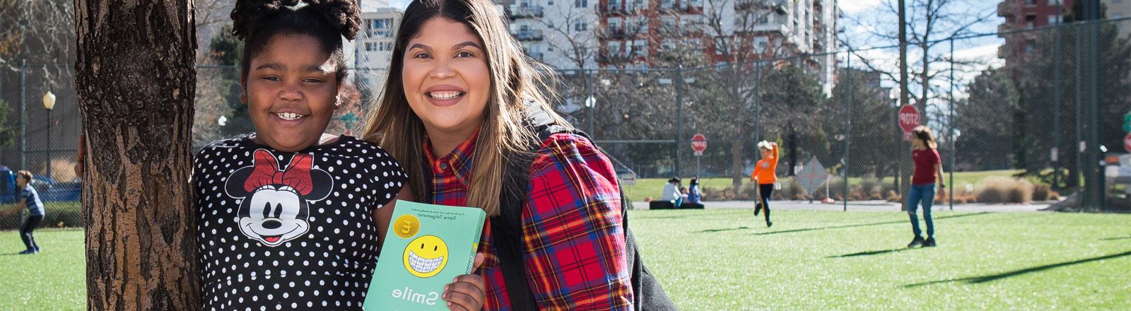 Center for Urban Education teacher standing outside with student holding a book