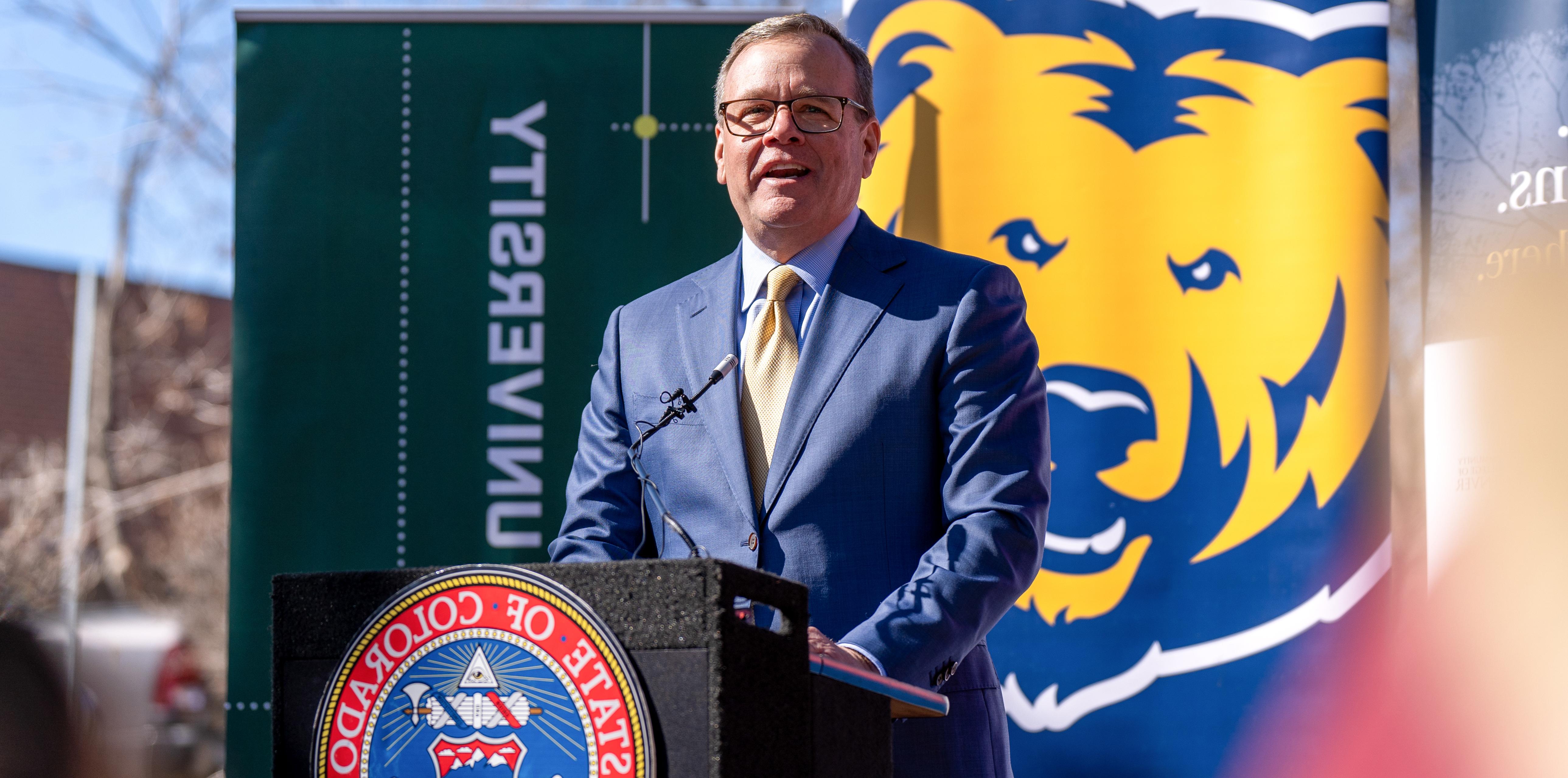 President Andy Feinstein st和ing outside behind a podium speaking to a crowd about the proposed legislation