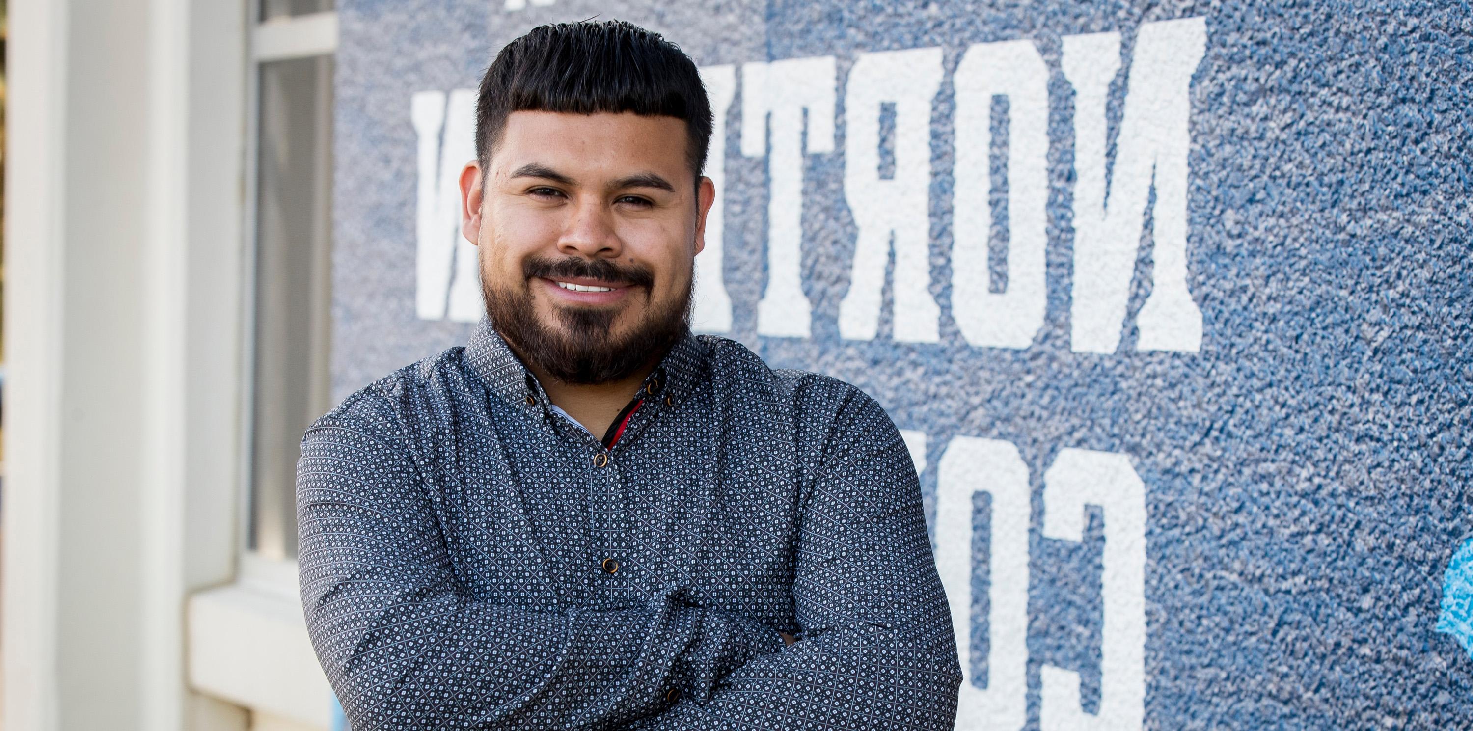 Fernando standing against a wall with his arms crossed smiling